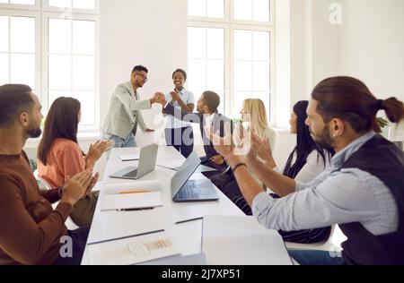 L'uomo felice scrolla le mani con il suo collega mentre il team aziendale è applaudente Foto Stock