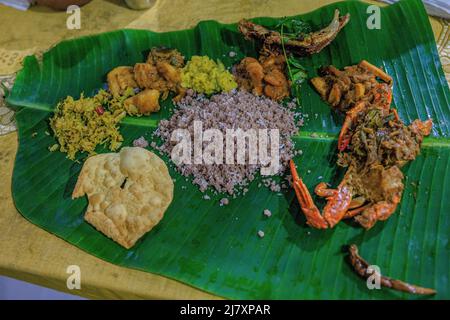 tradizionale pasto jaffna di pittu servito su una foglia di banana circondata da curry di granchio jaffna, pesce locale, curry di gamberi, patate vegetali e papadomo Foto Stock