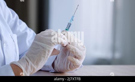 Primo piano dettaglio delle mani femminili in guanti di lattice donna irriconoscibile medico infermiere medico che tiene la siringa con vaccino di medicina liquida Foto Stock