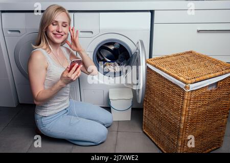 Ragazza giovane con un telefono in lavanderia cestino di lavanderia sporco Foto Stock