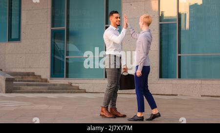 Due amici colleghi multirazziale business co-lavoratori arabo ispanico uomo e donna caucasica si incontrano all'aperto in strada facendo alta cinque mani gesto Foto Stock