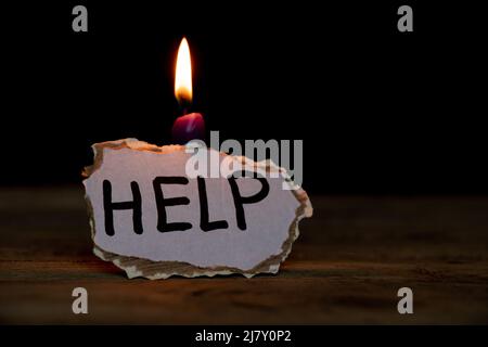 Carta di cartone con aiuto di testo si trova vicino ad una candela al buio su un tavolo a casa, un messaggio di aiuto per l'Ucraina nella guerra 2022 Foto Stock