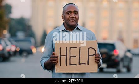 Triste stressato frustrato anziano afroamericano povero uomo età di pensionamento, turista perso, tenendo striscione in cartone con iscrizione bisogno di aiuto chiede Foto Stock