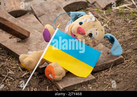 Un giocattolo per bambini sporco rotto e la bandiera dell'Ucraina si trova nel cortile durante la guerra in Ucraina, la morte di bambini per mano di soldie russo Foto Stock