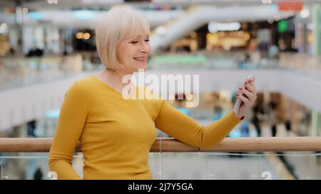 Donna matura di mezza età che tiene lo smartphone a portata di mano parlando con la videochiamata utilizzando l'app mobile per la conferenza sorridendo e salutando i gesti Foto Stock