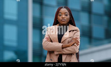 Seria concentrata giovane africana americana ragazza con acconciatura afro in piedi con le mani piegate, ritratto all'aperto. Professionale femminile nera focalizzata Foto Stock