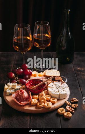 Salsiccia e formaggio tagliati con frutta, biscotti e salsa con due bicchieri di porto bianco e una bottiglia. Antipasto di vino, salumi e piatto di formaggi Foto Stock