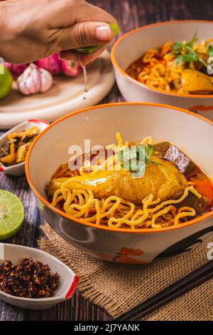 Spremere il limone per assaggiare, khao Soi Kai, delizioso cibo tailandese settentrionale, organizzato con condimenti sul tavolo. Foto Stock