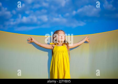 Ragazza Ucraina di 7 anni, è una patriota di Ucraina, vestita con un abito giallo contro un cielo blu. Cielo blu. Giorno di sole. Bambini ucraini gratis. CHIL Foto Stock