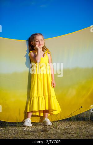 Ragazza Ucraina di 7 anni, è una patriota di Ucraina, vestita con un abito giallo contro un cielo blu. Cielo blu. Giorno di sole. Bambini ucraini gratis. CHIL Foto Stock
