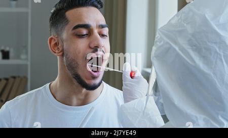 Infermiera irriconoscibile che fa il test pcr con l'apparecchiatura per il coronavirus covid-19 al tipo etnico. Primo piano uomo spagnolo arabo paziente maschio Foto Stock