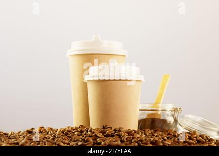 Caffè da asporto. Due tazze di cartone ecologico monouso su chicchi di caffè naturali su sfondo neutro chiaro con spazio per la copia. Caffè a. Foto Stock