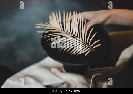 le mani femminili reggono un piatto di ceramica nera decorato con foglie di felce primo piano. Foto Stock