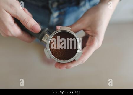 Il barista tiene in mano un portafiltro per preparare il caffè con una macchina per il caffè. Il processo di preparazione del cuppuccino. mano con manomissione Foto Stock