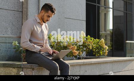 Giovane uomo d'affari formale user manager studente lavoratore seduto in terrazza vicino all'ufficio dell'azienda edificio in strada all'aperto con notebook studiare Foto Stock