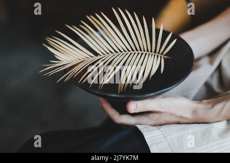 mani femminili che reggono un piatto in ceramica nera decorato con un primo piano di foglie di felce Foto Stock