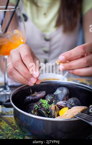 Una giovane donna mangia pesce e beve un cocktail. Il concetto di una vacanza in mare. Foto verticale. Foto Stock