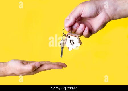 Acquisto di una casa. L'acquirente riceve la chiave per la proprietà. Appartamento ipotecario. Chiavi e una piccola casa in legno in mano. Consegna delle chiavi all'Ora Foto Stock