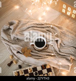 una tazza di caffè su una plaid beige lavorato a maglia con luci bokeh Foto Stock