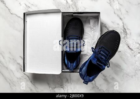 Un paio di nuove sneaker in tessuto mesh nella scatola aperta su un pavimento in marmo. Sneaker in tessuto blu nero con chiusura con lacci per uno stile di vita attivo e il fitness. Foto Stock