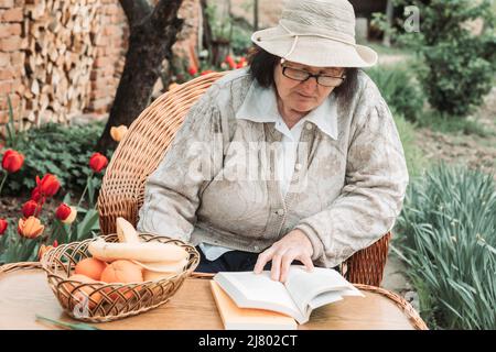 Donna anziana che si rilassa e legge un libro in giardino. Foto Stock