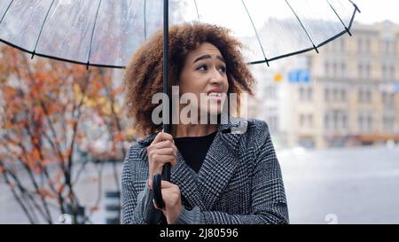 African American ragazza felice donna donna turista donna si leva in piedi forte vento pioggia tempesta freddo vento autunno tempo fuori in città strada con Foto Stock