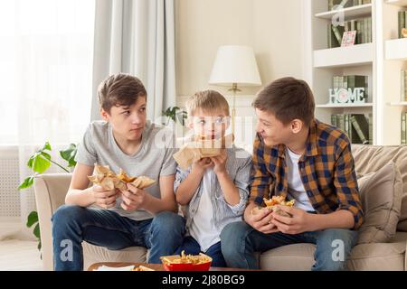 Un felice tre ragazzi adolescenti, mangiando fast food in soggiorno Foto Stock