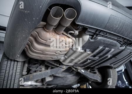 Primo piano dettaglio vista dal basso del tubo di scarico in metallo della parte dell'auto con macchie arrugginite. Manutenzione del veicolo sollevato, riparazione e riparazione su Foto Stock