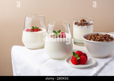 yogurt con lamponi e granola in bicchieri su un tavolo bianco Foto Stock