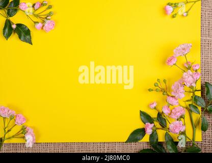 Composizione del bordo della cornice Roses. Piccole rose rosa su uno sfondo giallo isolato. Vista dall'alto con spazio di copia. Carta floreale. Concetto di modello di vacanza. Foto Stock