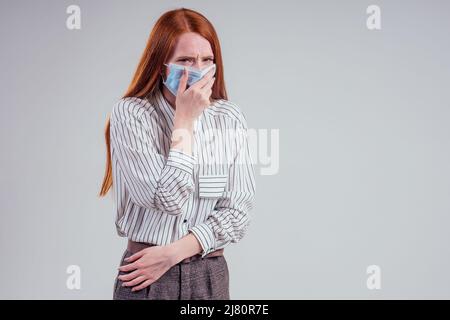 infelice rosso donna verde occhi donne d'affari in una camicia a righe indossando garza blu maschera bianco sfondo studio Foto Stock