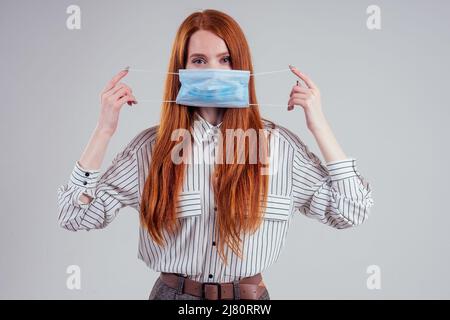 infelice rosso donna verde occhi donne d'affari in una camicia a righe indossando garza blu maschera bianco sfondo studio Foto Stock