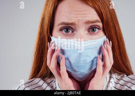 infelice rosso donna verde occhi donne d'affari in una camicia a righe indossando garza blu maschera bianco sfondo studio Foto Stock