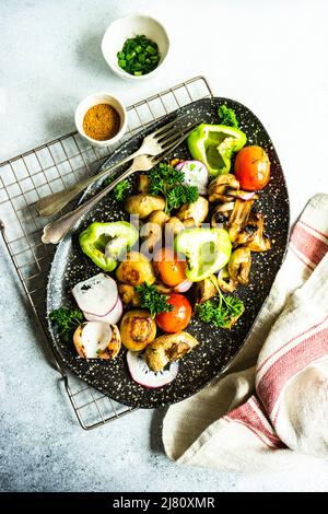 Vista dall'alto di un piatto di peperoni grigliati, funghi, pomodori, ravanelli, cipolle e prezzemolo con cipolla primaverile Foto Stock
