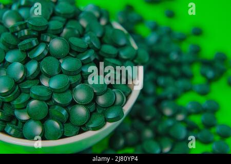 Spirulina pillole in una ciotola rotonda. Compresse di spirulina verde su sfondo verde. Compresse di alghe Spirulina. Vitamine e supplementi dietetici.Super cibo Foto Stock