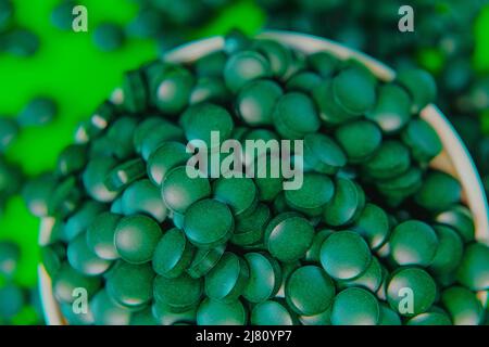 Spirulina pillole in una ciotola rotonda. Compresse di spirulina verde su sfondo verde. Compresse di alghe Spirulina. Vitamine e supplementi dietetici.Super cibo Foto Stock