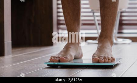 Primo piano gambe maschio sottile sportivo sottile irriconoscibile ragazzo maschio atleta in piedi a casa bagno a piedi nudi camminare su bilance elettroniche controllo peso Foto Stock