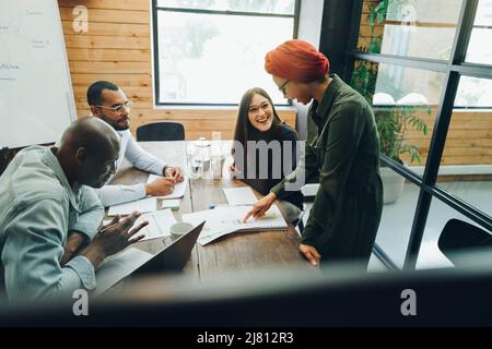 Un team aziendale diversificato che discute di un documento di report durante una riunione della sala riunioni. Gruppo di professionisti multiculturali che condividono idee creative in Foto Stock
