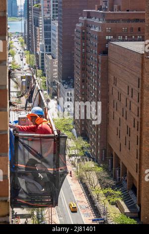 Lavoratori edili in alto sopra una strada urbana a New York City in un paniere sospeso, Midtown Manhattan, USA 2022 Foto Stock