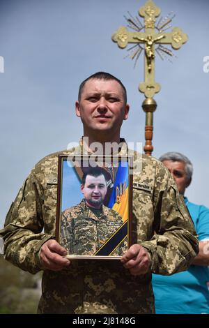 Kulchytsi, Ucraina. 11th maggio 2022. Un uomo militare tiene un ritratto di un soldato maggiore Petro Sarakulo, morto nella regione di Donetsk a causa dell'invasione militare dell'Ucraina da parte della Russia durante i suoi funerali nel villaggio di Kulchytsia, regione di Lviv funerali del soldato maggiore Petro Sarakulo nel suo villaggio natale di Kulchytsi, regione di Lviv. A causa dell'invasione militare russa dell'Ucraina il 24 febbraio 2022, andò a servire nelle forze Armate dell'Ucraina. Morì il 5 maggio nella regione di Donetsk durante una battaglia con gli occupanti russi. Il defunto è sopravvissuto da sua moglie e da due figli - figlia mi Foto Stock