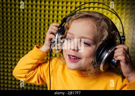 ragazza bionda ricurly capelli stile star cantante artista in una blusa gialla con cuffia registrazione nuova canzone con microfono. Foto Stock