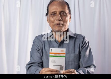 Un vecchio indiano sorridendo con carta Aadhaar in mani su sfondo bianco Foto Stock