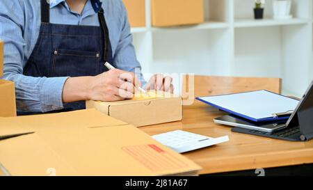 Il proprietario del negozio maschile che ha imballato il pacchetto ordine cliente per la consegna nel suo magazzino. Immagine ritagliata Foto Stock