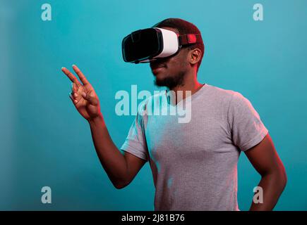 Modello emozionato che si diverte con le cuffie per realtà virtuale interattive, che utilizzano la tecnologia moderna con la visione futuristica 3D. Occhiali da gioco per adulti da millennial con simulazione visiva per il tempo libero. Foto Stock