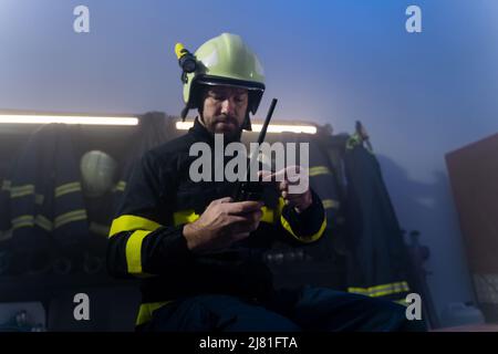 Vigile del fuoco maturo che si prepara all'azione nella stazione dei vigili del fuoco di notte. Foto Stock