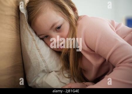 Piccola ragazza triste con sindrome di Down che si trova a letto a casa. Foto Stock