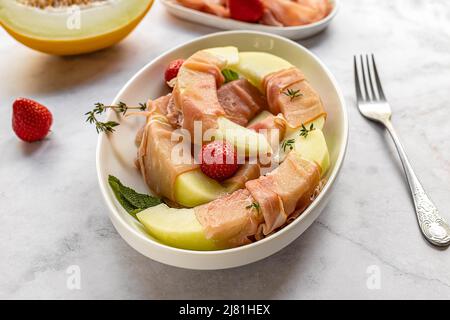 Melone di miele con fragola e prosciutto. Snack gourmet, gustoso antipasto, cibi dolci e salati. Foto Stock