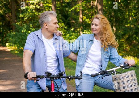 Concetto attivo di vecchiaia, gente e lifestyle felice coppia senior in bicicletta nel parco estivo in una giornata di sole in abiti casual confortevole, godere la vita e il tempo trascorso insieme Foto Stock