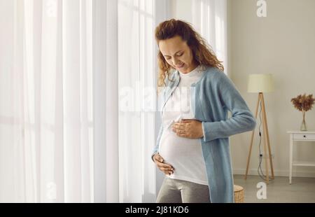 Felice donna incinta giovane che tocca il ventre ammirazioni e gode interessante periodo della sua vita. Foto Stock