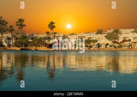 Edifici, sedie a sdraio e ombrelloni si riflettono nella calma acqua di mare sulla spiaggia nella città di resort al mattino a Sharm El Sheikh durante il sole Foto Stock